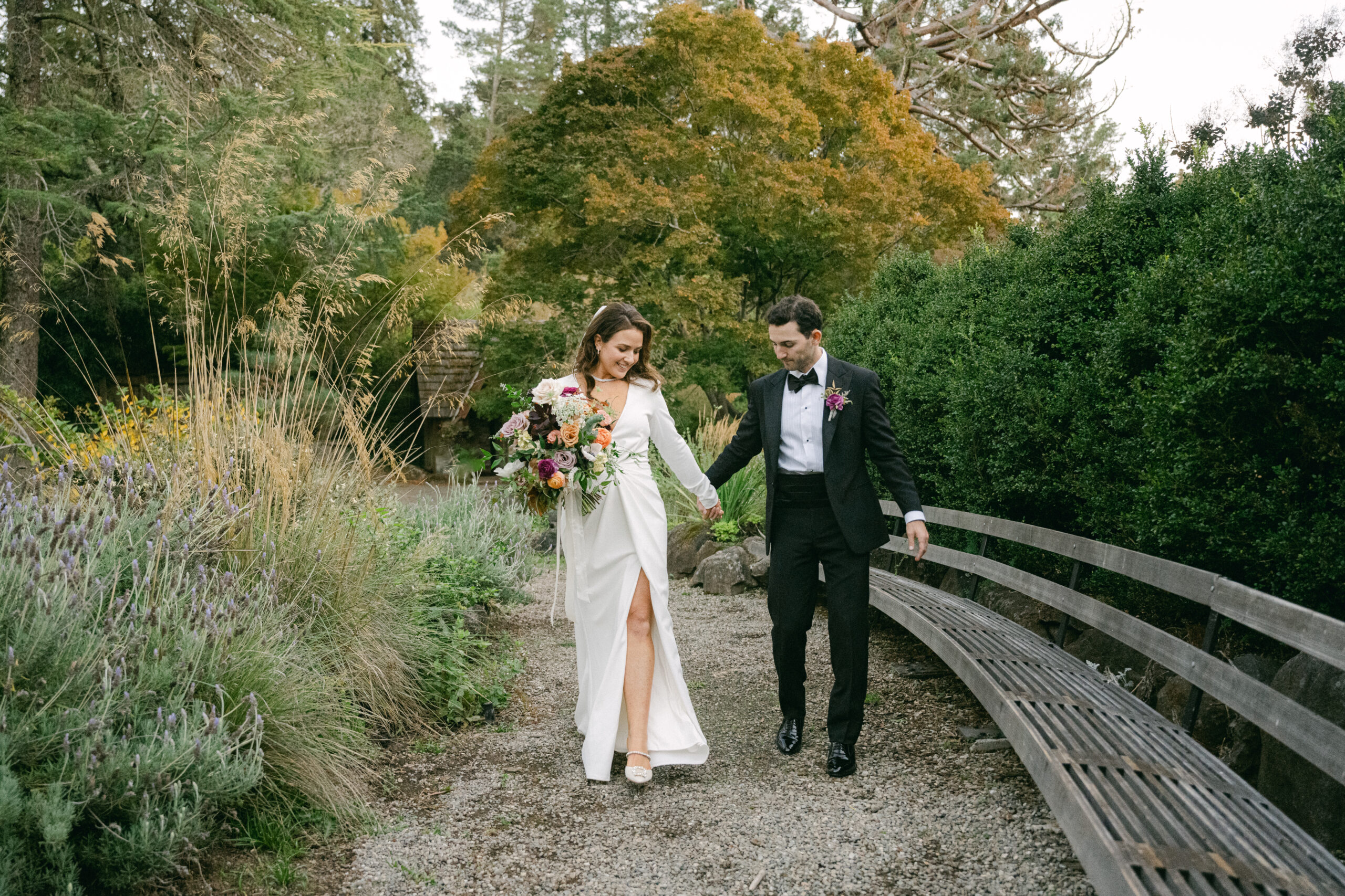 bride and groom walk through garden holding hands