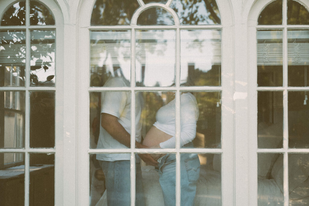 Intimate at-home maternity session with cozy setting through bedroom window in bay area