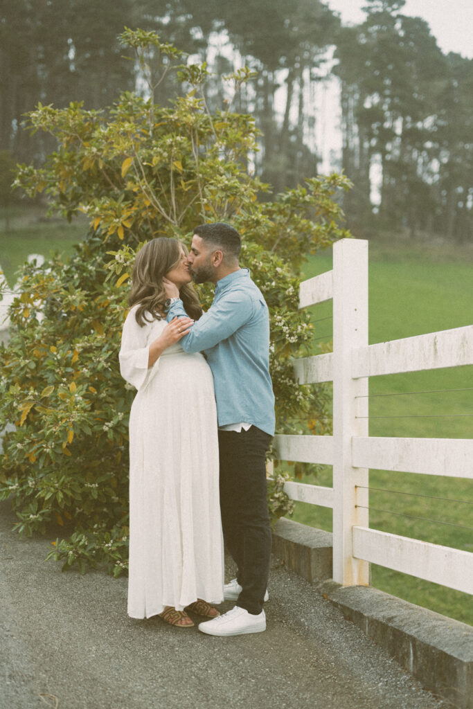 Outdoor maternity portrait with couple kissing in front of fence