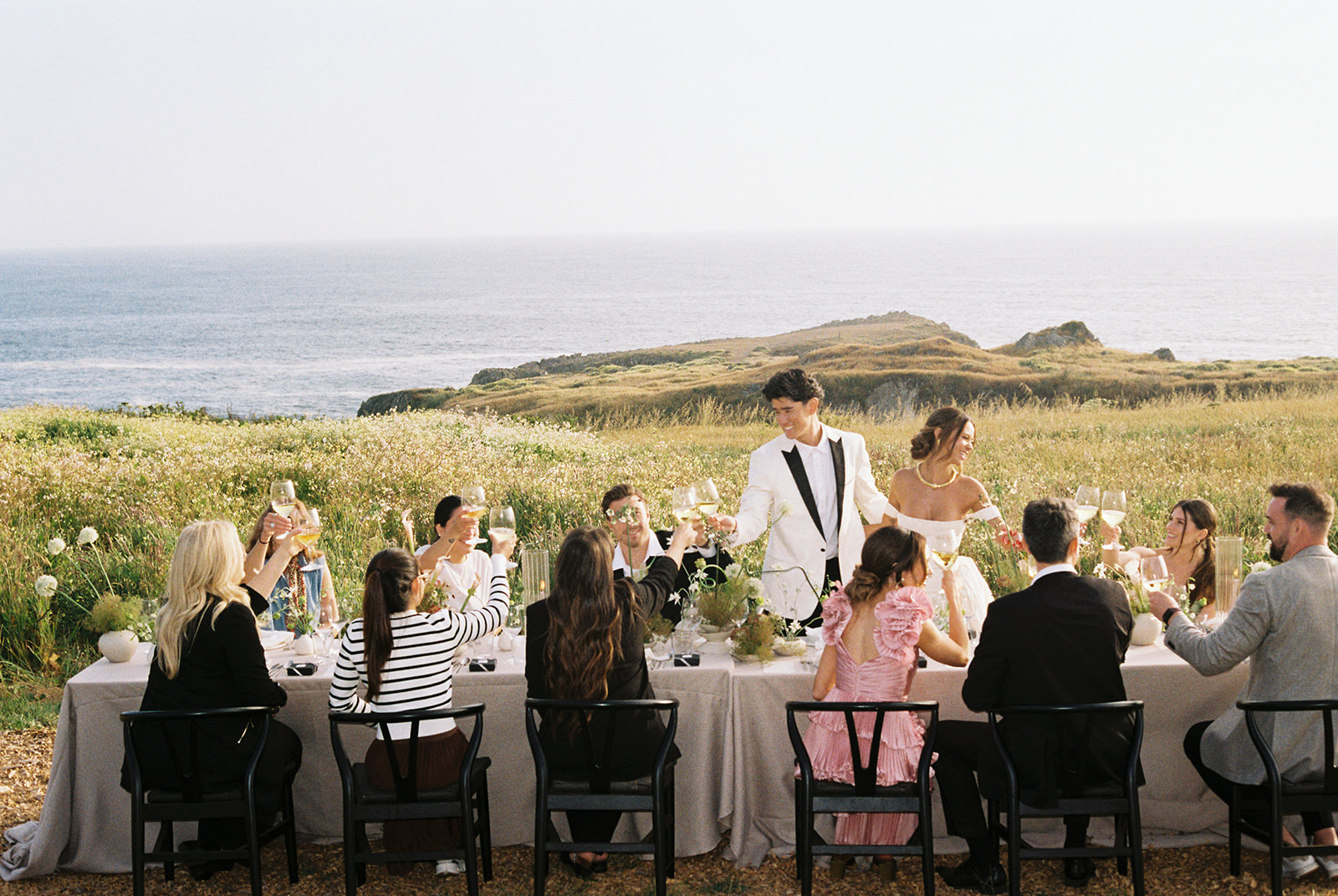 Couple cheers with guests on cliffside with panoramic ocean views at Sea Ranch Lodge