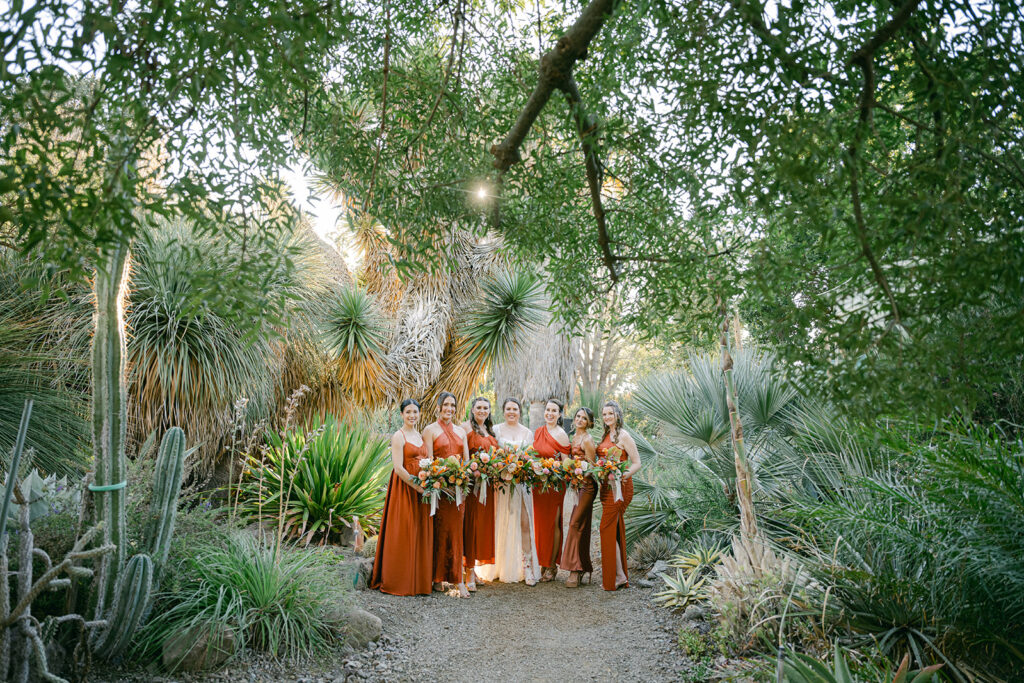 wedding party lines up in garden path with flowers for smiling wedding photo