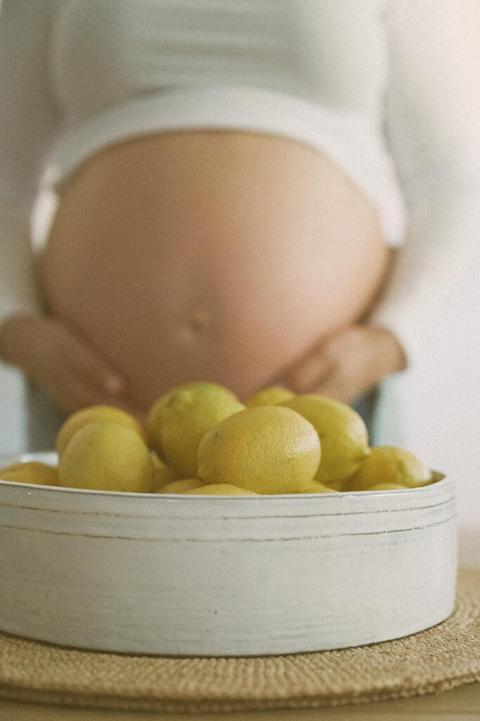 close up of pregnant belly with bowl of lemons during in-home maternity photography session
