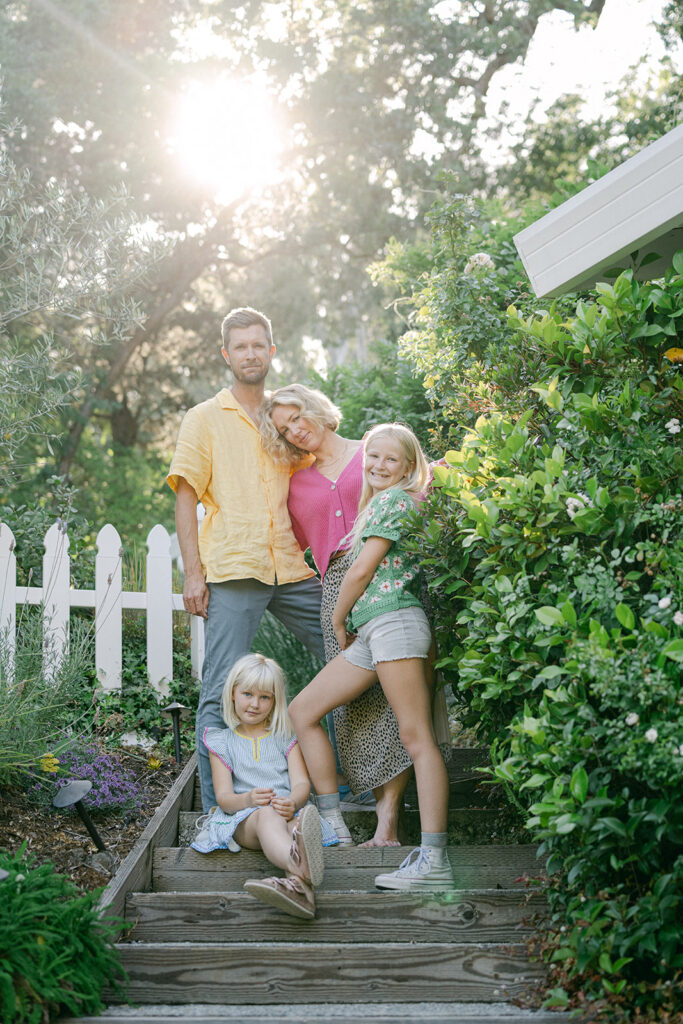 family of four standing together on garden steps outside home during outdoor family photography session