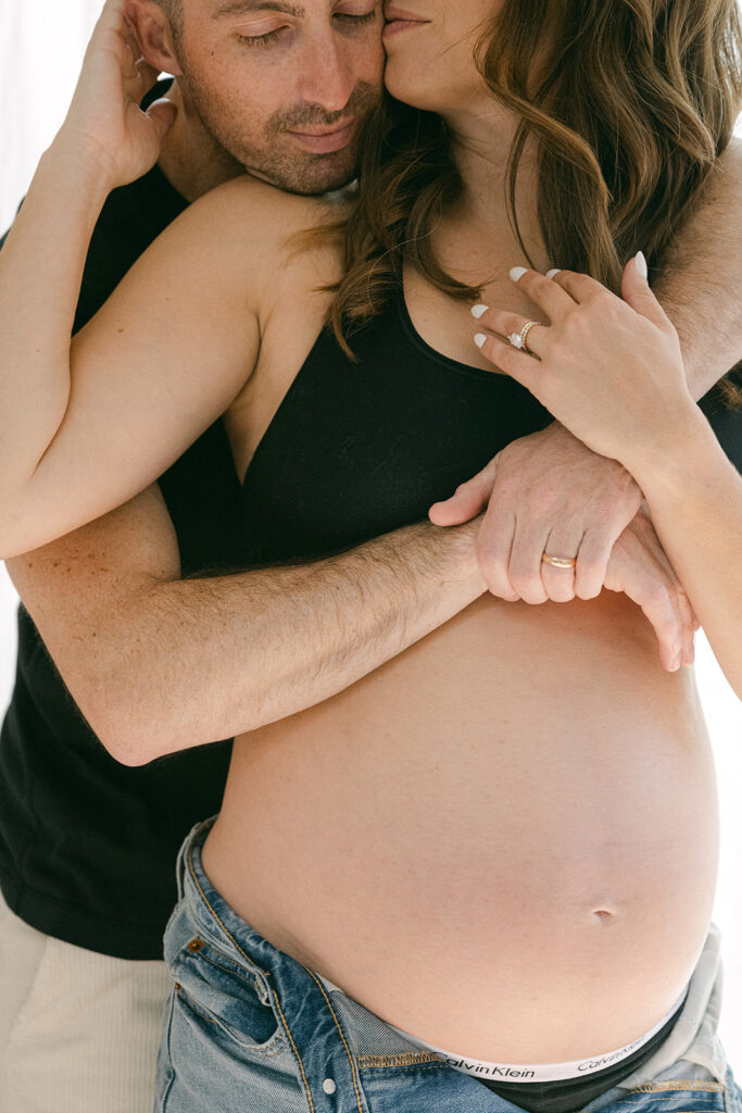 couple embracing pregnant belly during in-home maternity photography session