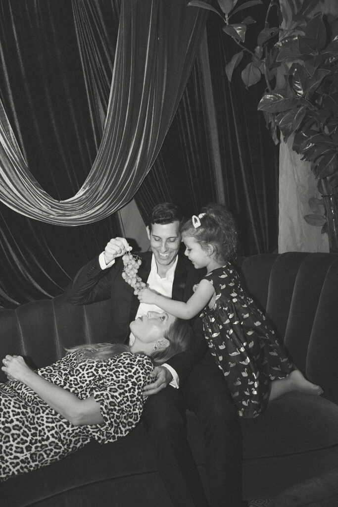 family sitting on couch while child feeds grapes to parent during playful lifestyle family photography session