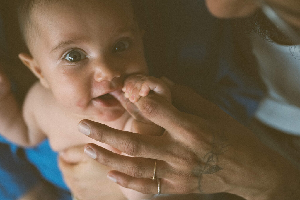 baby holding parent’s fingers in soft natural light during close up in-home family session