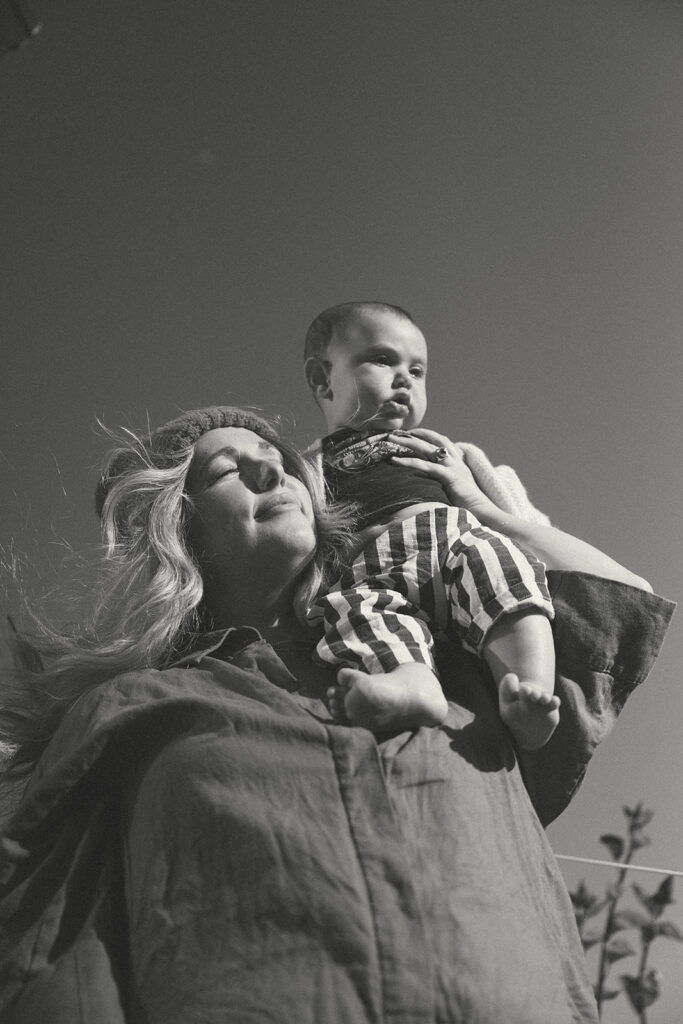 mother holding baby outdoors looking upward during candid family photography session