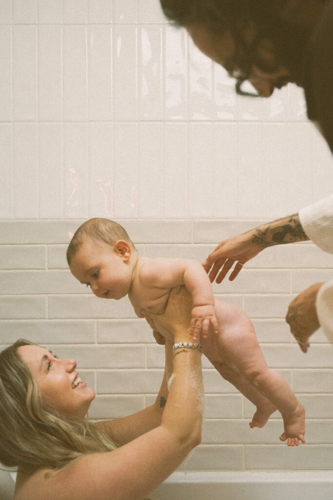 mother lifting baby in bath while smiling during candid in-home family photography session