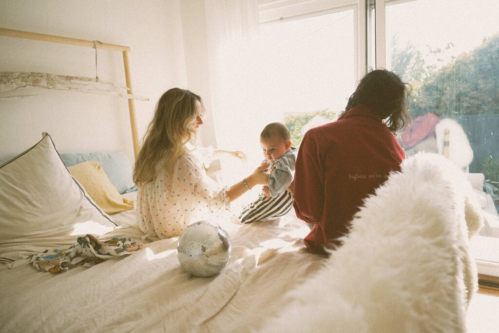 in-home family photography session in the Bay Area with parents sitting on bed with baby in natural window light
